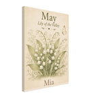 A vertical canvas wall art print featuring a vintage-style botanical illustration of lily of the valley flowers with the text 'May', 'Lily of the Valley', and the name 'Mia' on a warm cream background.