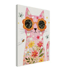 A vertical canvas wall art print featuring a whimsical pink cat decorated with flowers and wearing orange flower-shaped sunglasses with black starry lenses. The background of the artwork is white, and the canvas is shown at a slight angle against a solid white background.
