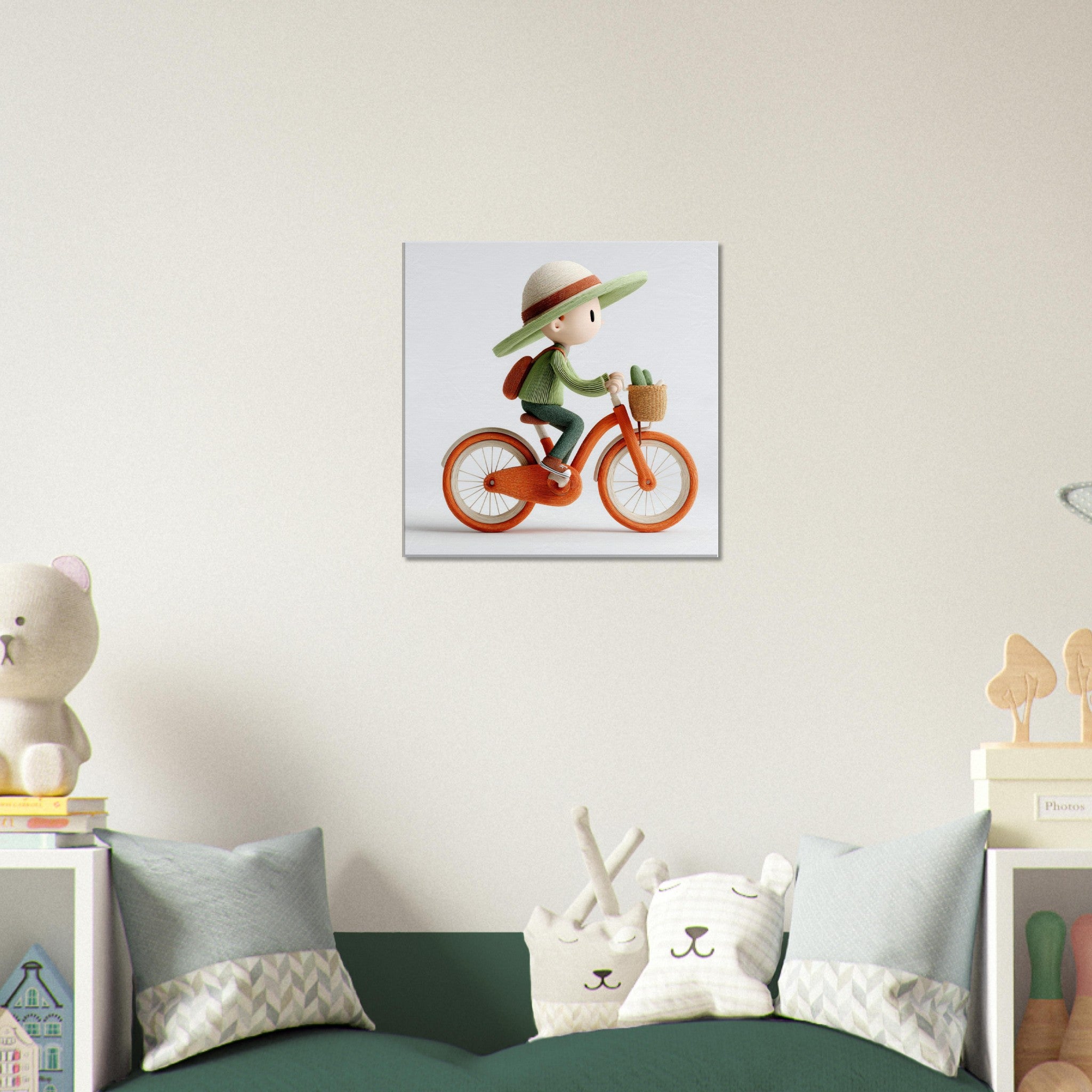 A square wall art print showing a cartoon child riding an orange bicycle, displayed above a green sofa in a styled children's room with pillows and toys.
