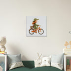 A square wall art print showing a child riding an orange bicycle with a basket, displayed above a green sofa in a styled children's room with pillows and toys.