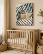 A styled nursery scene featuring a wooden baby crib with a beige blanket, a woven basket with a stuffed cat, and a matching cat-shaped plush on the floor. Above the crib hangs a square canvas painting of a striped cat reading a book against blue and cream stripes.