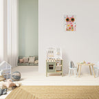 A styled children's playroom with a floral cat wall art print hanging on a white wall above a small wooden play kitchen, chair, and table. The room features light wood floors, a woven rug, and a soft green accent wall in the background.