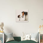 A square wall art print featuring a whimsical illustration of a small girl with dark hair and a brown horse at a stable, displayed on a light beige wall above a green sofa with decorative pillows in a styled children's room.