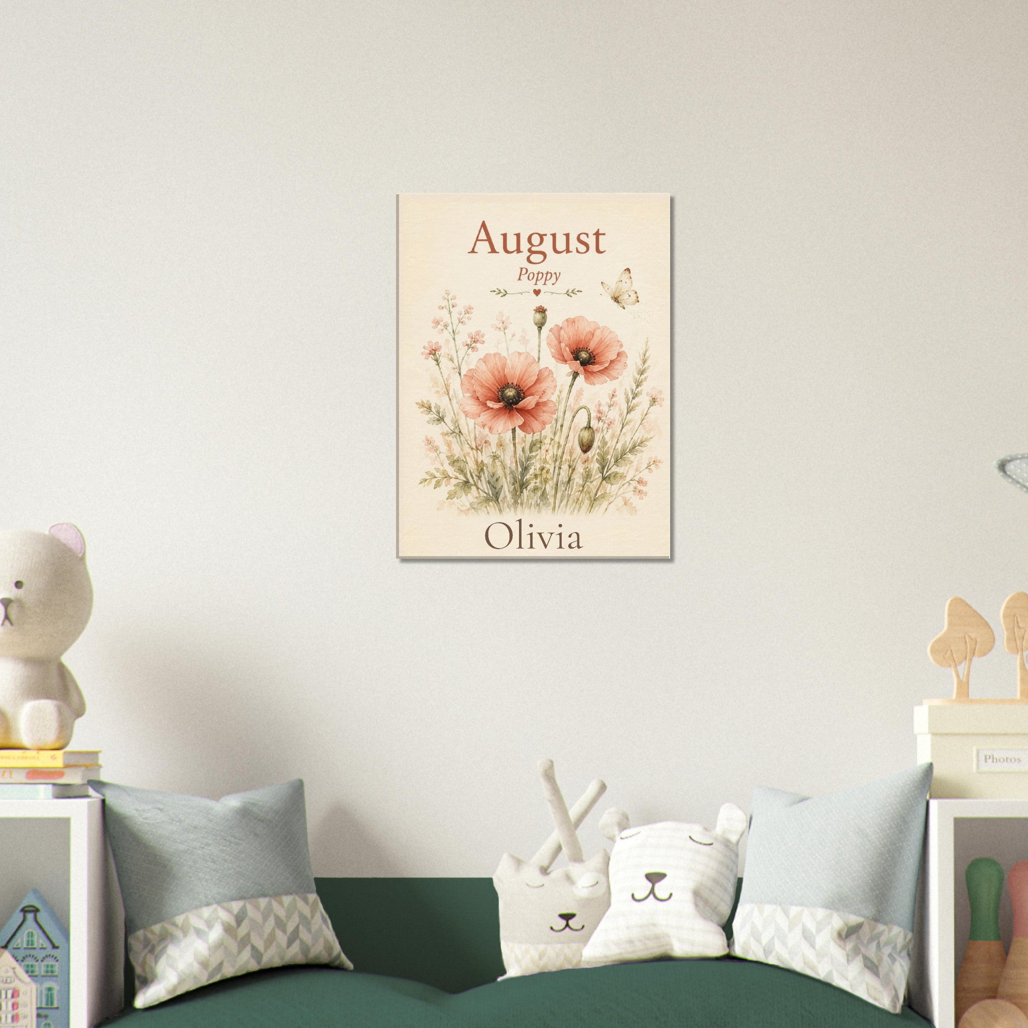 A personalized vertical floral art print for a baby girl, featuring the text 'August Olivia' and watercolor poppy illustrations, displayed on a wall above a green sofa in a styled nursery setting.