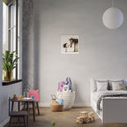 A styled children's bedroom featuring a small framed art print of a horse and a child on the wall above a white bed. The room includes a small wooden table with a pink cushion, a white basket filled with plush toys, a potted plant by the window, and a hanging white globe lamp.